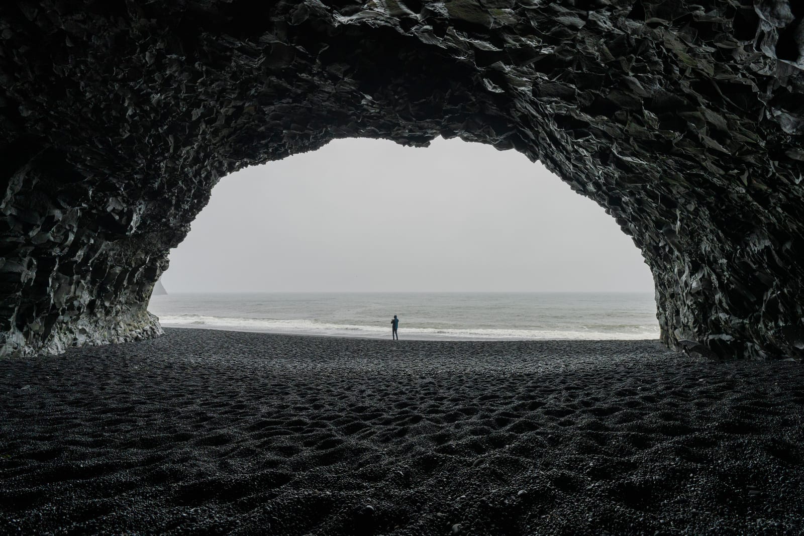 Black cave mouth framing a tiny figure on the beach.