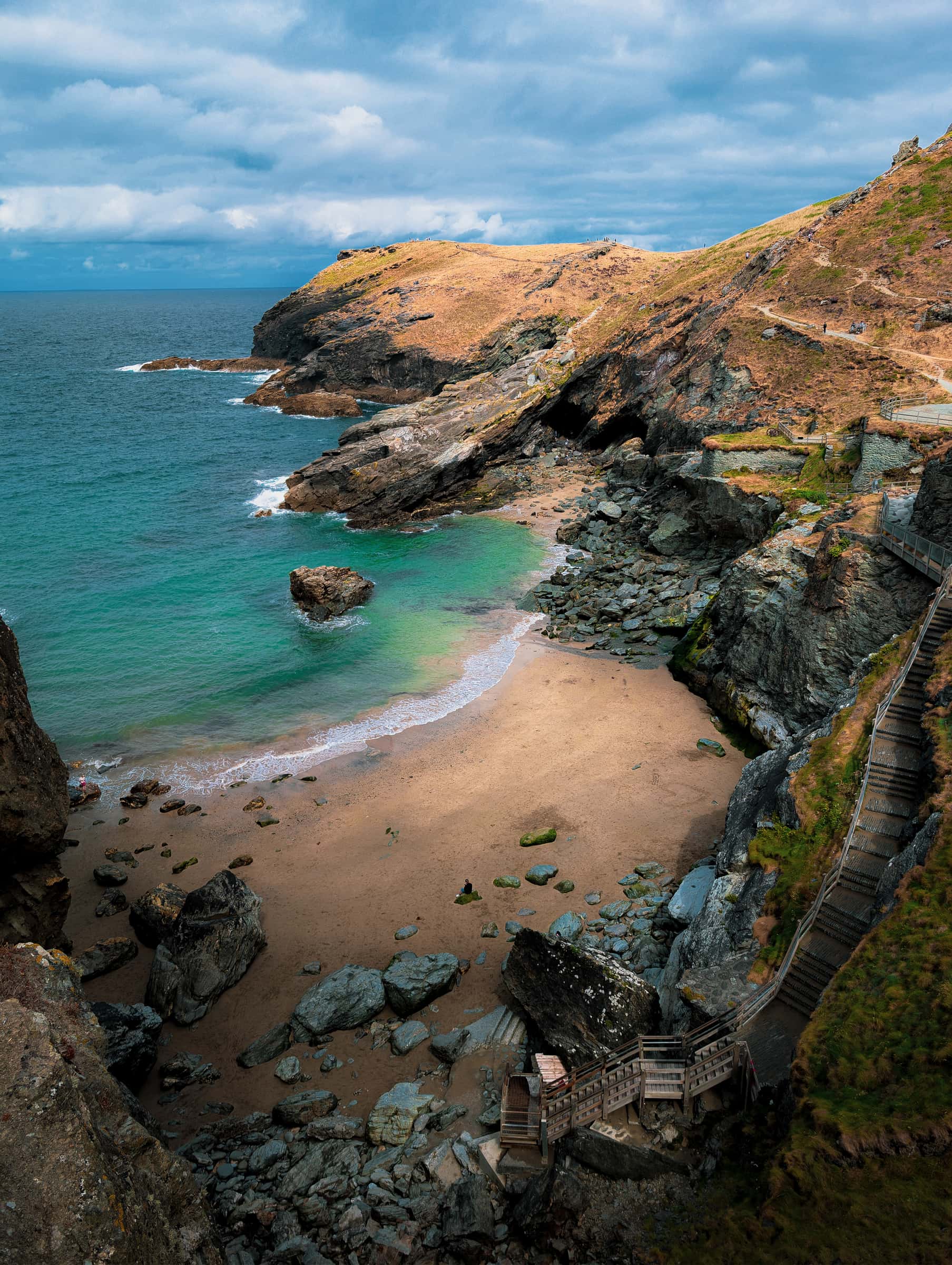 Turquoise cove with sandy beach, cliffs and wooden steps along the coast path.
